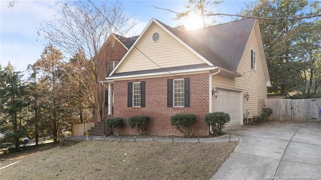 view of home's exterior featuring a garage, concrete driveway, brick siding, and fence