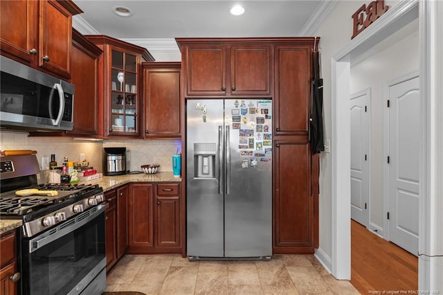 kitchen featuring light stone counters, crown molding, tasteful backsplash, appliances with stainless steel finishes, and glass insert cabinets