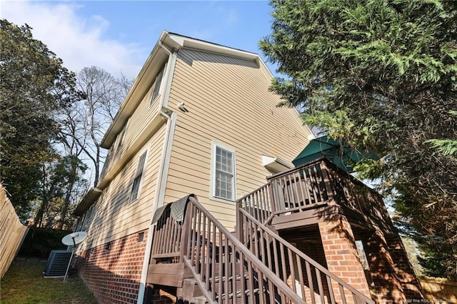 view of property exterior with brick siding, stairway, a wooden deck, and fence