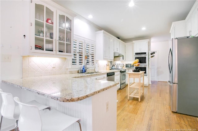 kitchen with light wood-style floors, appliances with stainless steel finishes, a peninsula, under cabinet range hood, and a sink