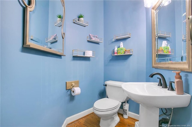 half bath with toilet, baseboards, and wood finished floors