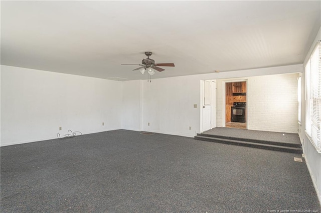 carpeted spare room featuring brick wall and a ceiling fan