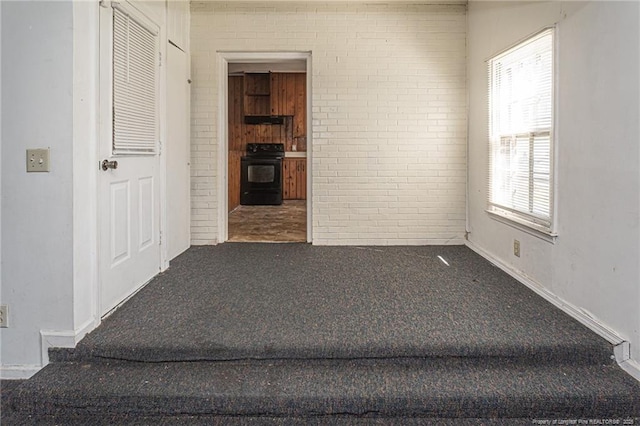 unfurnished room featuring brick wall and carpet floors