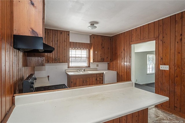 kitchen with wood walls, under cabinet range hood, brown cabinets, and electric range oven