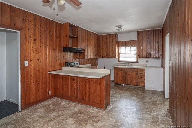 kitchen with wooden walls, brown cabinetry, under cabinet range hood, open shelves, and a sink