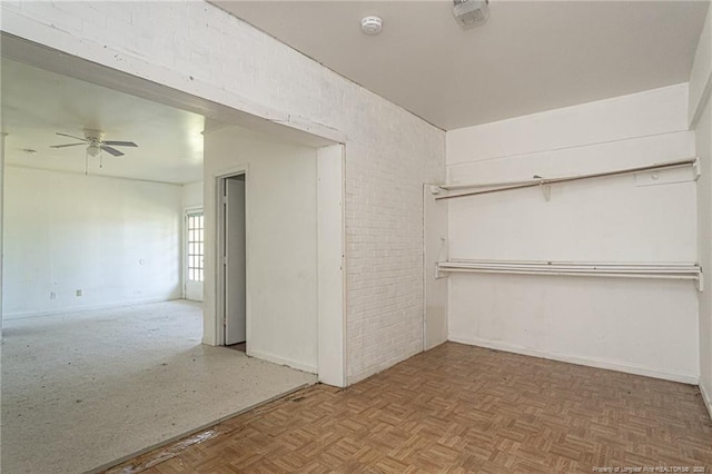 spare room with brick wall, a ceiling fan, and baseboards