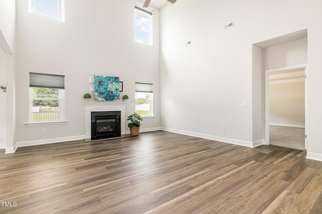 unfurnished living room with a towering ceiling, ceiling fan, wood finished floors, a fireplace with flush hearth, and baseboards