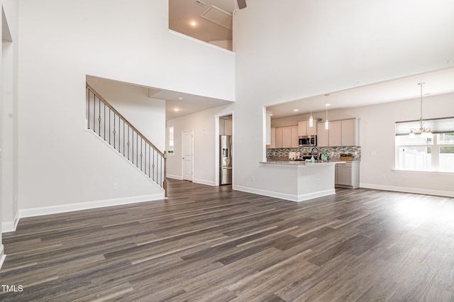 unfurnished living room with dark wood-style flooring, baseboards, stairway, recessed lighting, and a chandelier