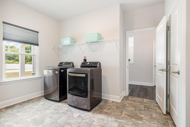 washroom featuring washing machine and clothes dryer, baseboards, and light stone finish floors