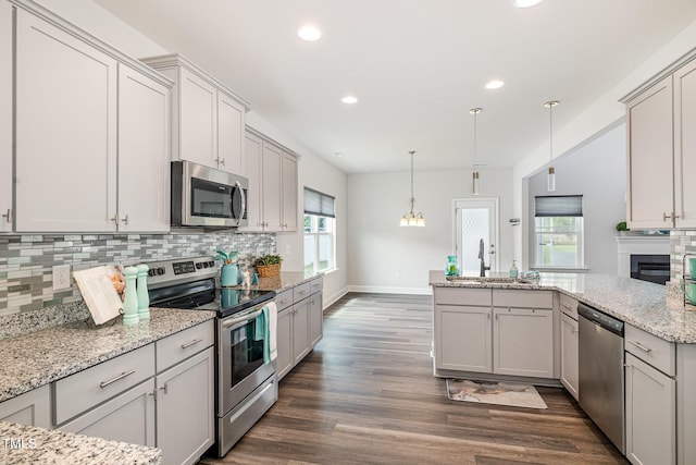 kitchen with appliances with stainless steel finishes, a sink, backsplash, dark wood finished floors, and a peninsula