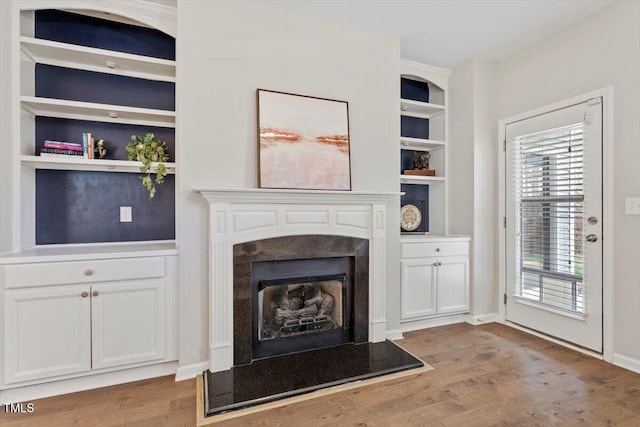 unfurnished living room featuring baseboards, wood finished floors, a high end fireplace, and built in features