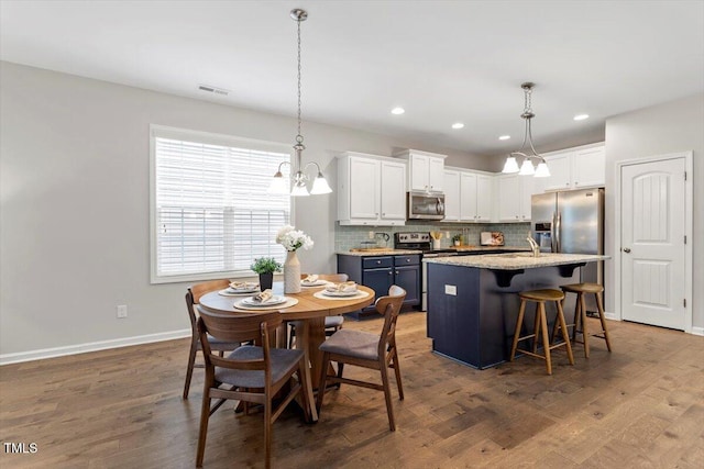 kitchen with wood finished floors, white cabinetry, visible vents, appliances with stainless steel finishes, and decorative backsplash