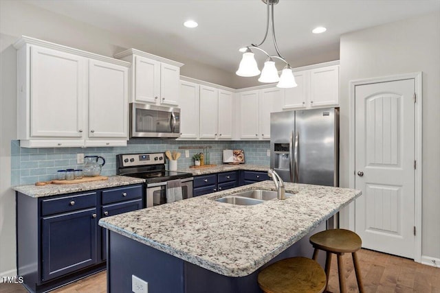 kitchen with a breakfast bar area, blue cabinetry, stainless steel appliances, white cabinets, and a sink