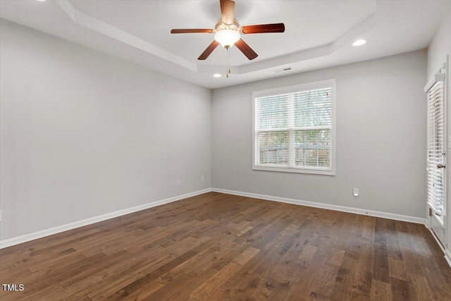 empty room with a tray ceiling, dark wood-type flooring, visible vents, and baseboards