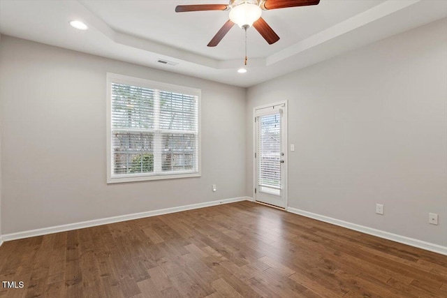 spare room with recessed lighting, a raised ceiling, visible vents, wood finished floors, and baseboards