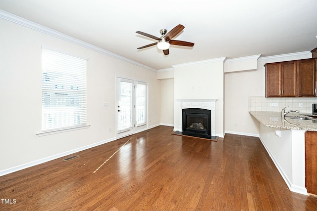 unfurnished living room with baseboards, visible vents, a fireplace with raised hearth, dark wood-style flooring, and crown molding