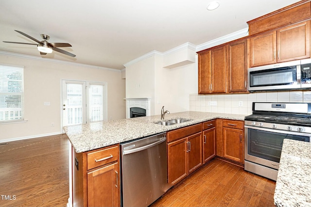 kitchen with dark wood finished floors, appliances with stainless steel finishes, ornamental molding, a peninsula, and a sink