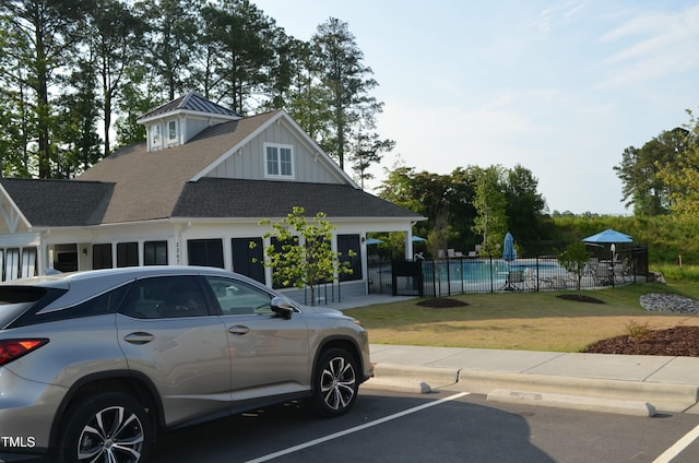 view of front facade featuring a fenced in pool, roof with shingles, fence, board and batten siding, and a front yard