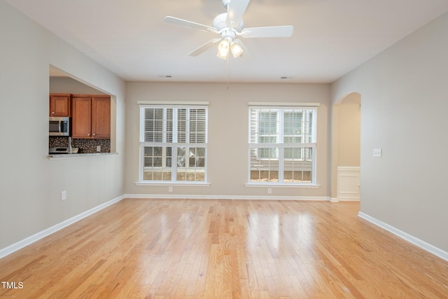 unfurnished room with arched walkways, light wood finished floors, a ceiling fan, and baseboards