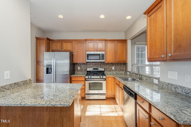 kitchen featuring appliances with stainless steel finishes, light wood-style floors, brown cabinetry, and a sink