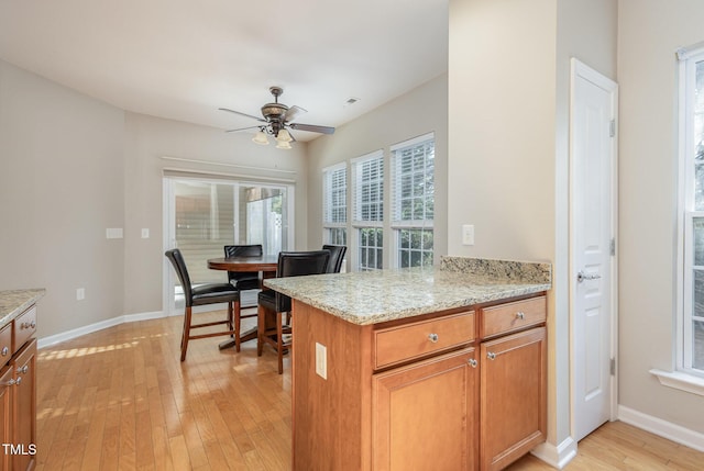 kitchen with light stone counters, light wood-style flooring, a ceiling fan, baseboards, and brown cabinetry