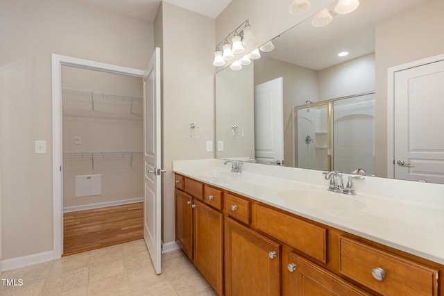 full bathroom with double vanity, a shower stall, a walk in closet, and a sink