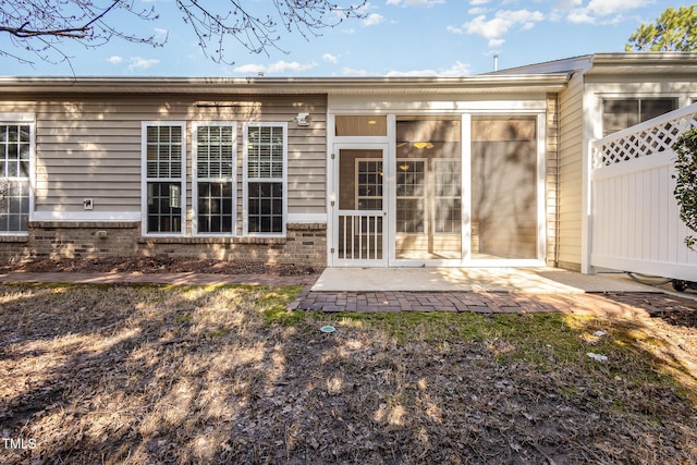 rear view of house featuring a sunroom, a patio area, fence, and brick siding