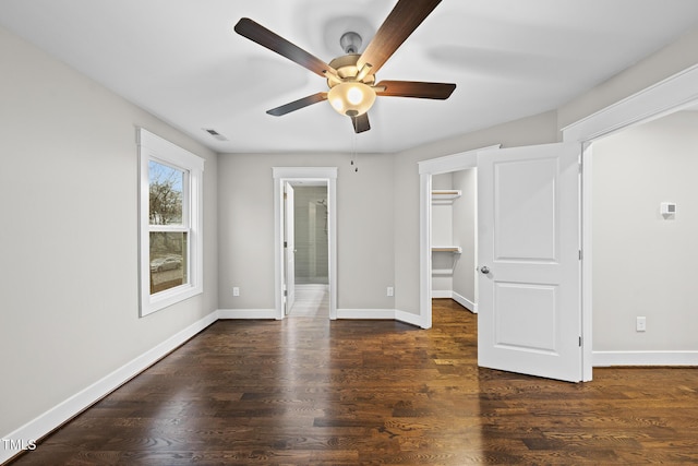 unfurnished bedroom with a walk in closet, baseboards, and wood finished floors