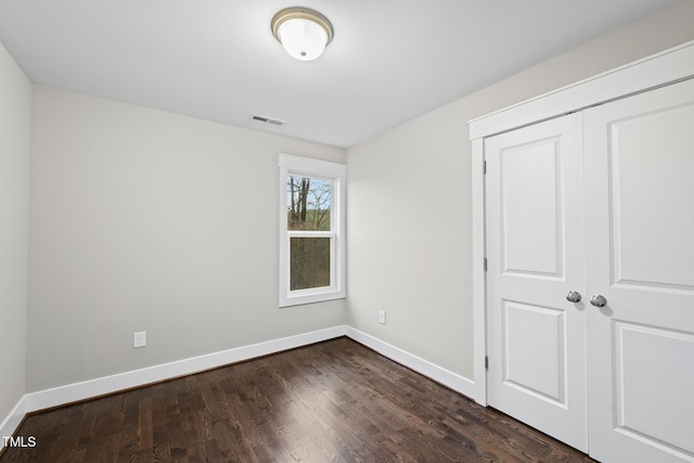 unfurnished bedroom with dark wood-type flooring, a closet, visible vents, and baseboards