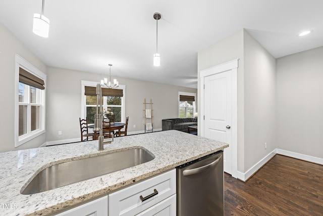 kitchen featuring light stone counters, dark wood-style flooring, hanging light fixtures, stainless steel dishwasher, and a sink