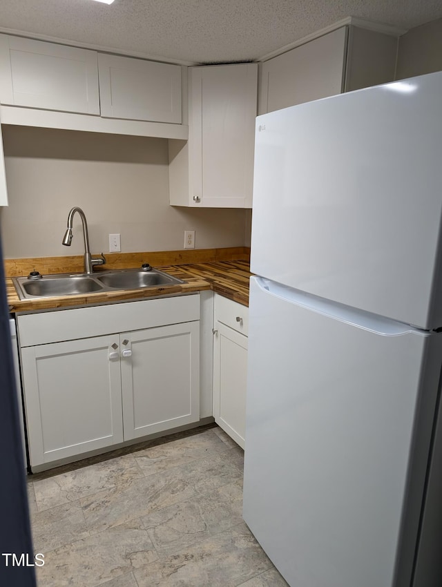 kitchen with freestanding refrigerator, white cabinets, a sink, a textured ceiling, and butcher block countertops