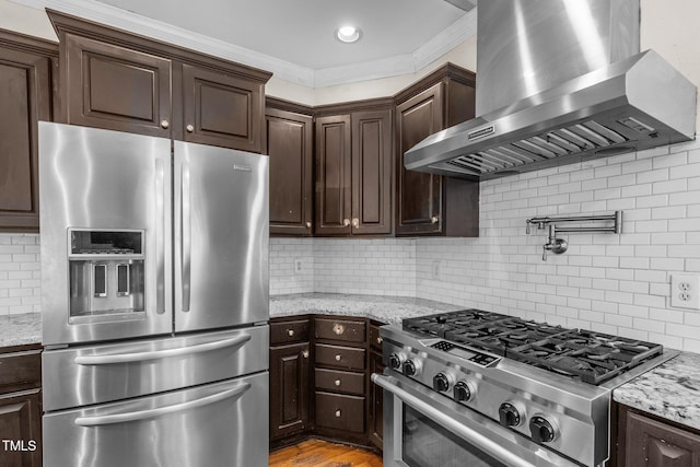 kitchen featuring dark brown cabinetry, appliances with stainless steel finishes, crown molding, wall chimney range hood, and backsplash