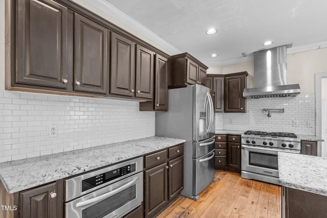 kitchen with wall chimney exhaust hood, stainless steel appliances, dark brown cabinets, crown molding, and light wood-type flooring