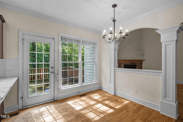 unfurnished dining area featuring a notable chandelier, visible vents, ornamental molding, light wood-type flooring, and ornate columns