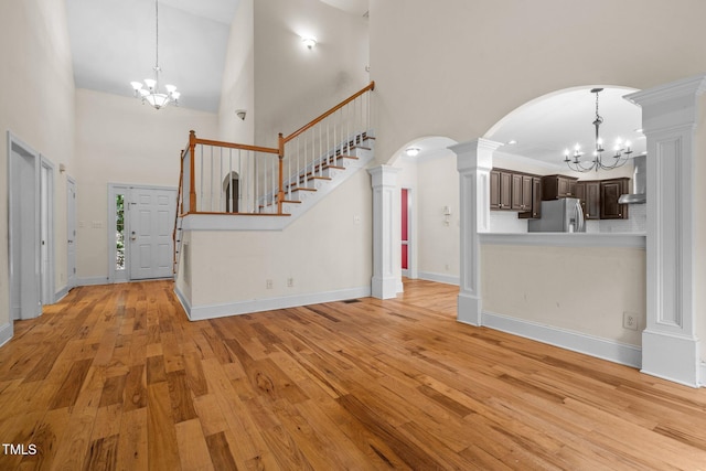 unfurnished living room with stairway, a chandelier, arched walkways, and ornate columns