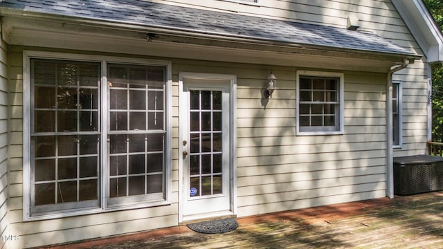 property entrance featuring roof with shingles and a deck