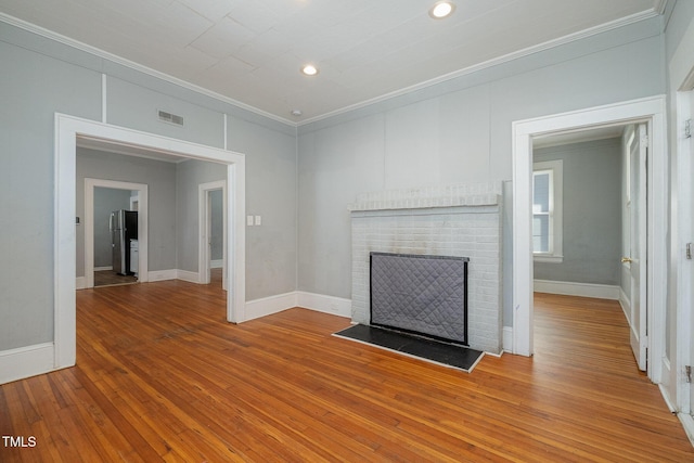 unfurnished living room with wood-type flooring, visible vents, ornamental molding, a brick fireplace, and baseboards