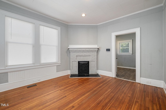 unfurnished living room with a brick fireplace, wood-type flooring, visible vents, and crown molding