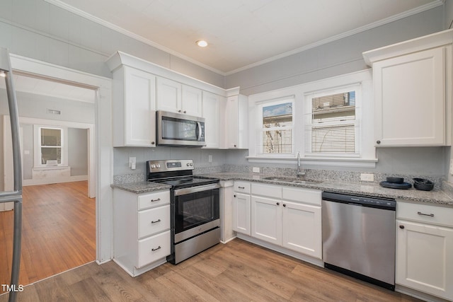 kitchen with ornamental molding, stainless steel appliances, light wood-type flooring, white cabinetry, and a sink