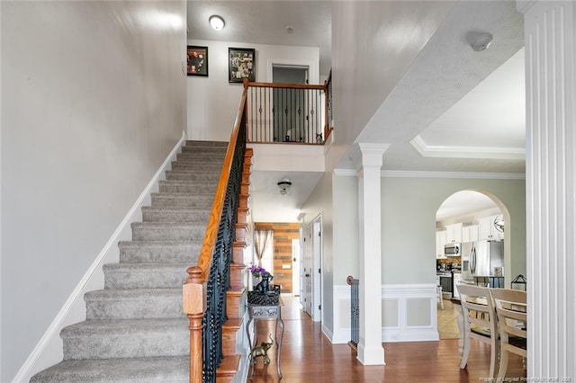 staircase with arched walkways, a raised ceiling, ornamental molding, wood finished floors, and ornate columns