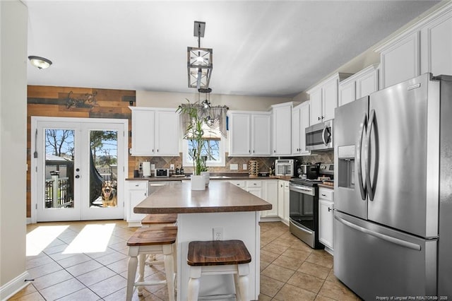 kitchen featuring light tile patterned floors, white cabinets, appliances with stainless steel finishes, decorative backsplash, and dark countertops