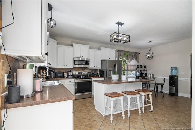 kitchen featuring dark countertops, backsplash, appliances with stainless steel finishes, a sink, and a kitchen island