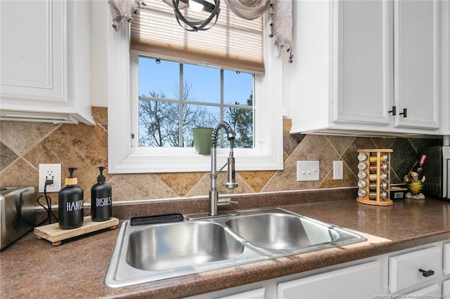 kitchen featuring tasteful backsplash, dark countertops, a sink, and white cabinetry