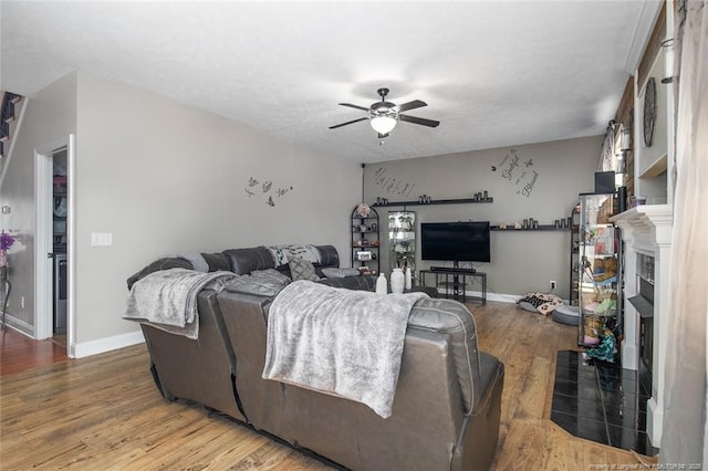 living area featuring a fireplace with flush hearth, ceiling fan, baseboards, and wood finished floors