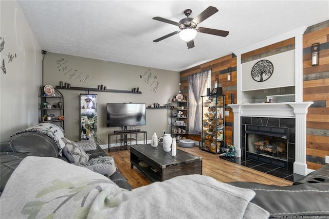 living room featuring a ceiling fan, a tile fireplace, wood walls, and wood finished floors