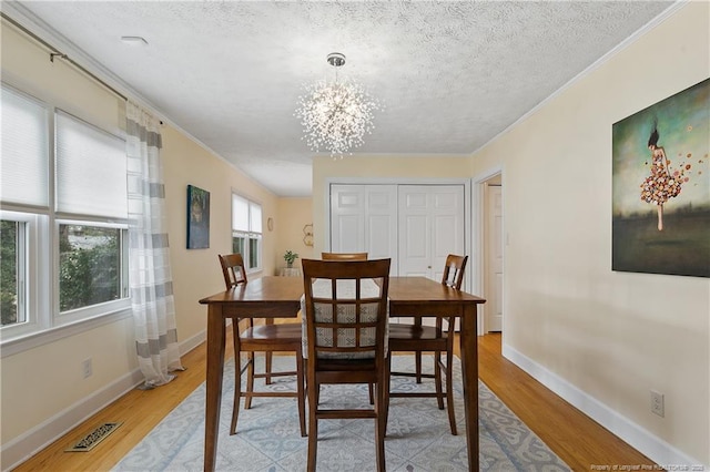 dining room featuring crown molding, visible vents, an inviting chandelier, light wood-style floors, and a textured ceiling