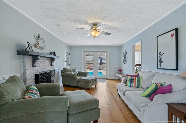 living room with a textured ceiling, wood finished floors, french doors, a brick fireplace, and crown molding