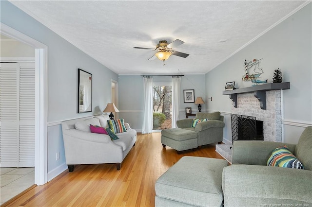 living room with light wood-style flooring, ceiling fan, ornamental molding, a textured ceiling, and a fireplace