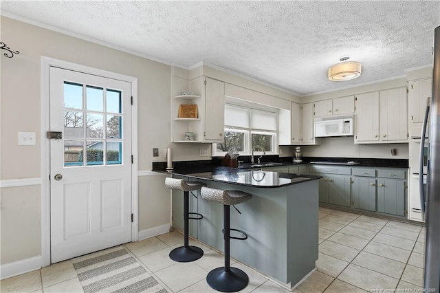 kitchen featuring dark countertops, white microwave, a peninsula, and a sink