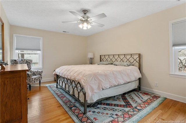 bedroom featuring light wood finished floors, baseboards, multiple windows, and visible vents